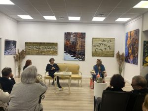 Wernisaż wystawy „Tańczące na wodzie" – goście słuchają rozmowy w galerii, w tle fotografie Ingrid Plater-Syberg i Moniki Krzakiewicz