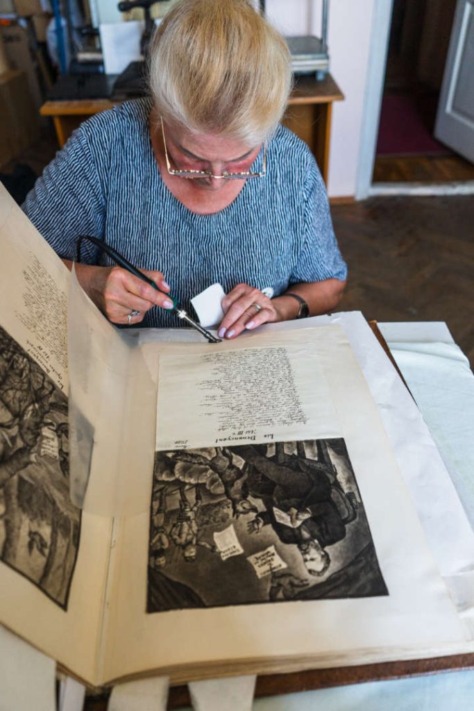 Lesia Dziendzieluk pracuje przy otwartym albumie, na stronie z ryciną Dzieduszyckiego, widok ogólny